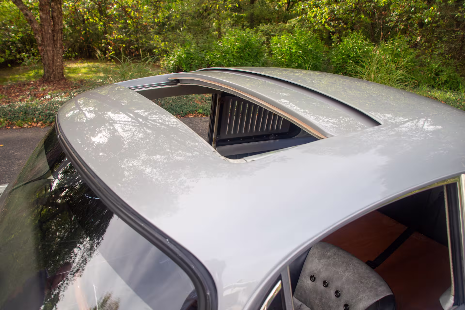 Close-up of a silver car roof with an open sunroof and a partial view of the interior seat.