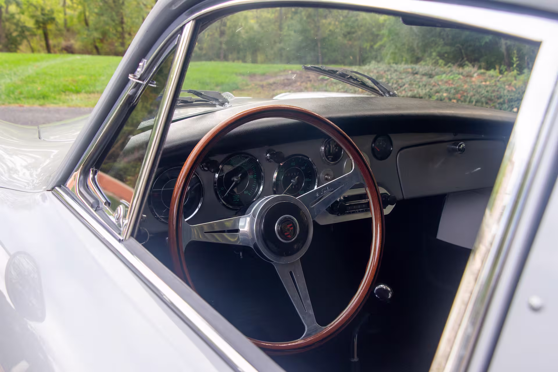 Interior of a vintage car showing a wooden steering wheel, dashboard with analog gauges, and a manual gear shift.