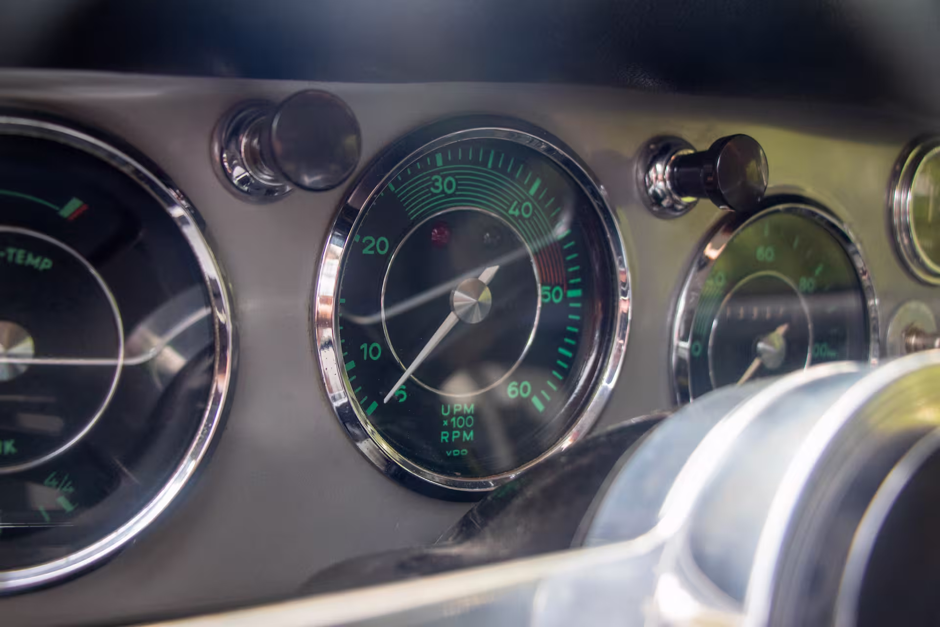 Close-up of classic car dashboard dials including a tachometer with green numerical markings and chrome trim.