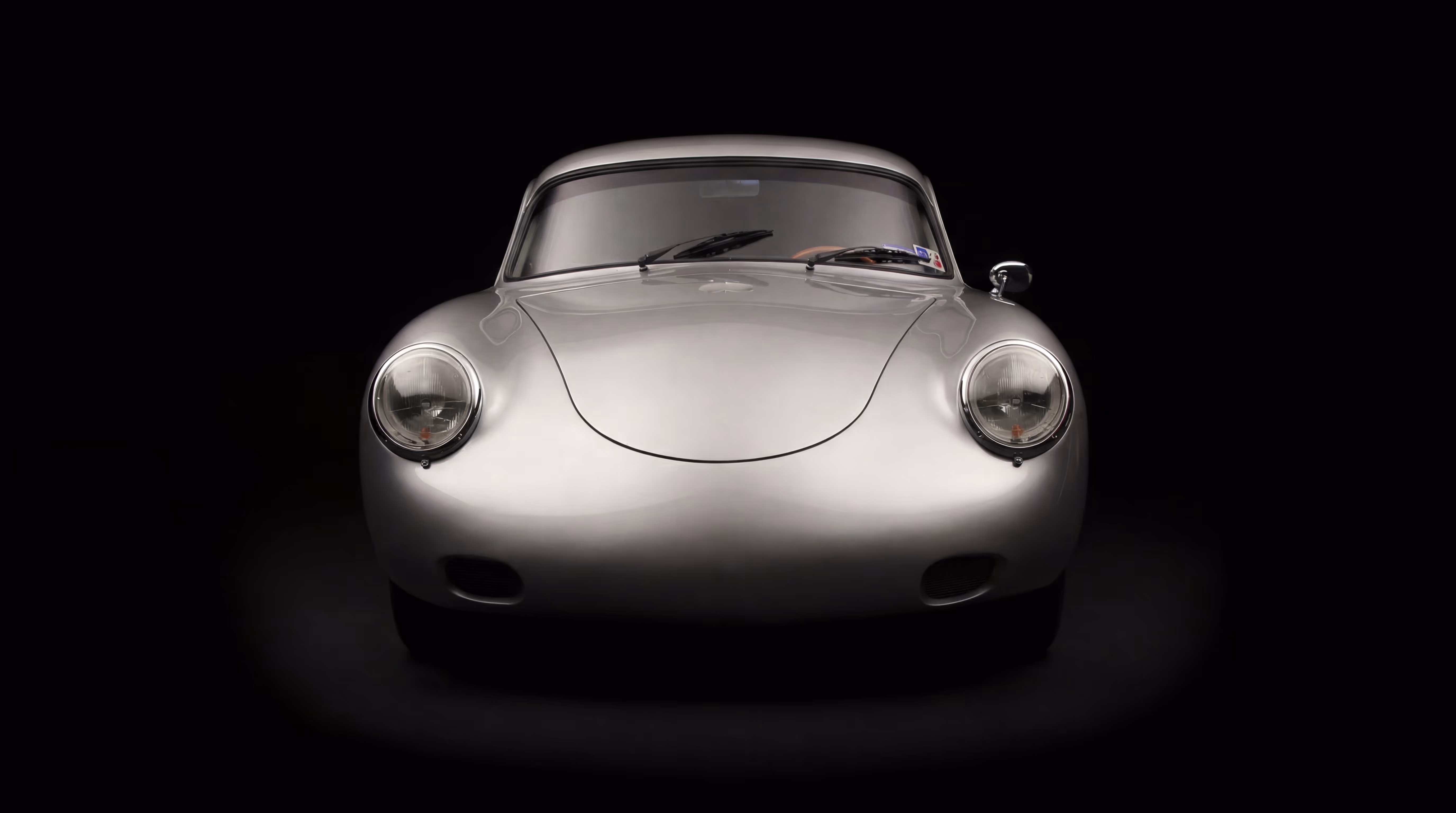 Front view of a classic silver Porsche car with round headlights against a black background.
