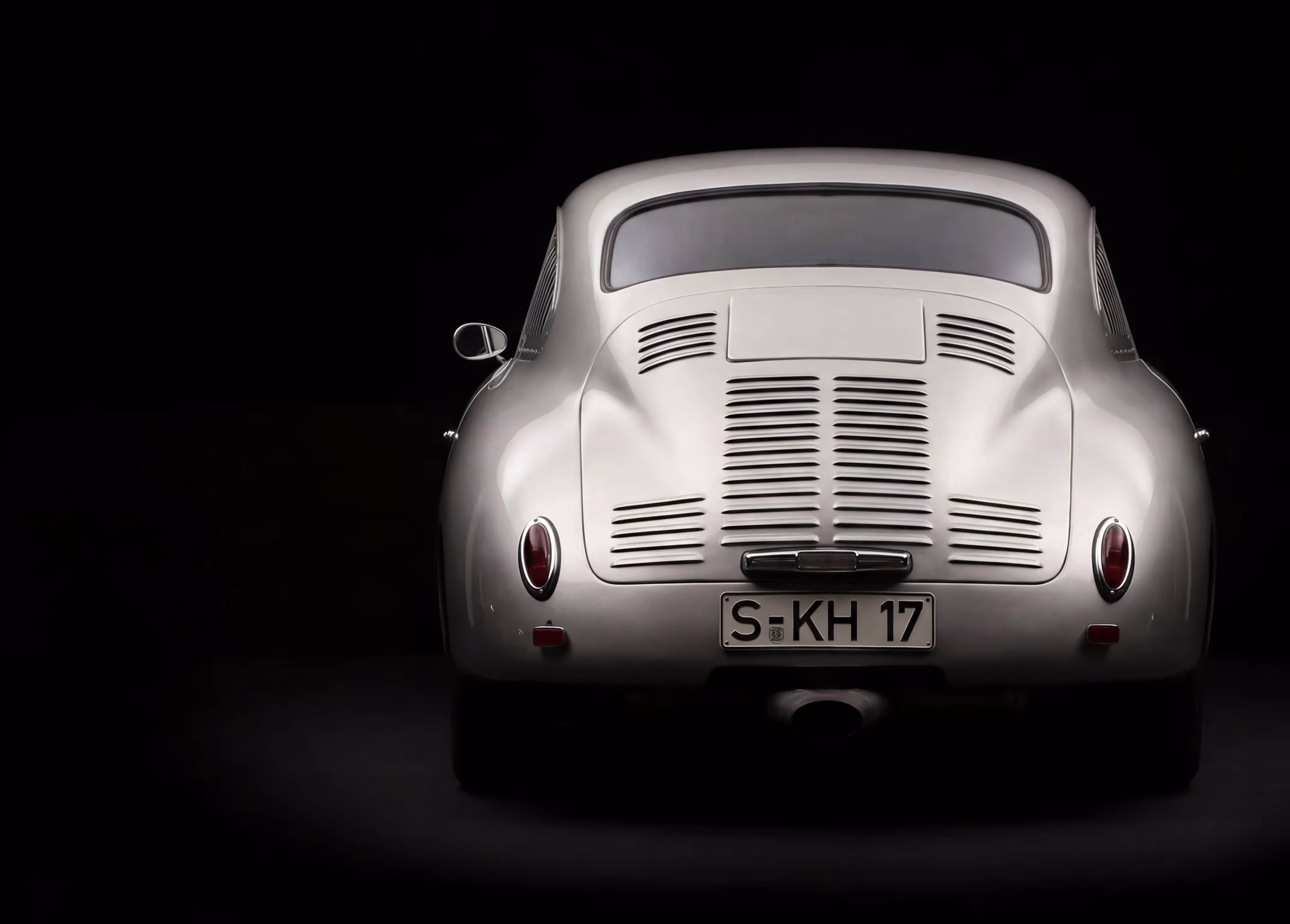 Classic silver Porsche car viewed from the rear against a black background.