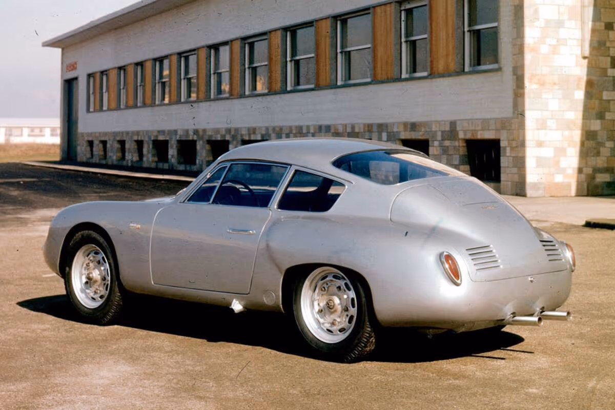 Silver vintage sports car parked outdoors beside a building with multiple windows.