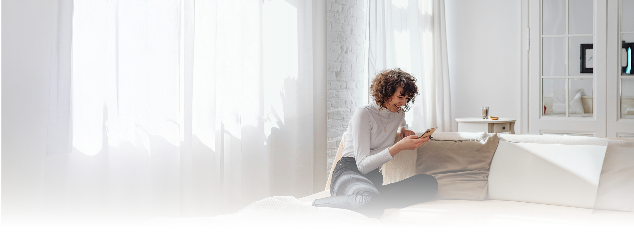 A renter sitting on a sofa checking her phone in a bright living room