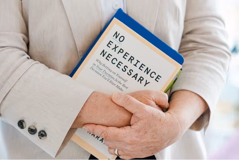 A person in a cream blazer holding Ronnen Harary's book No Experience Necessary against their chest
