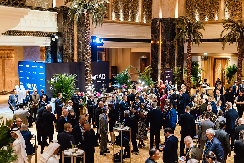 A crowd of MEAD Summit delegates in business attire gathered beneath palm trees and marble columns, with MEAD Abu Dhabi 2025 signage in the background
