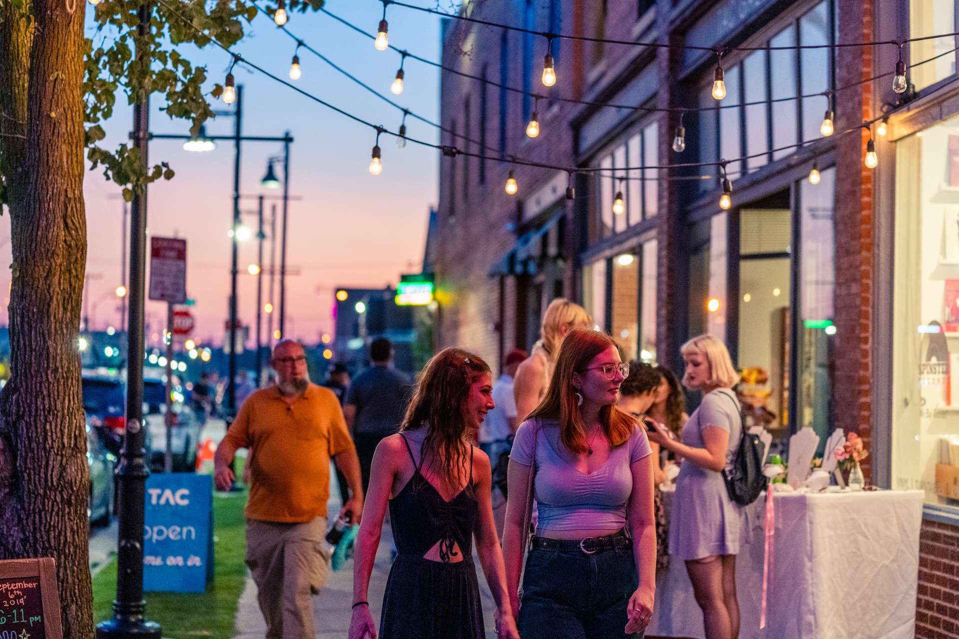 A bustling sidewalk in the downtown arts district on a warm summer night.
