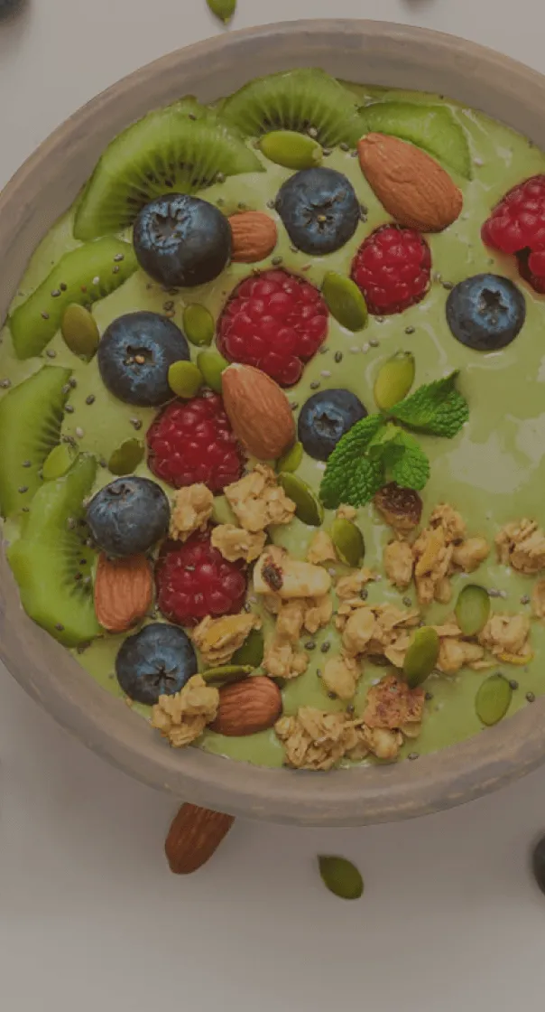 Miseczka zielonego smoothie z kiwi, borówkami, malinami, migdałami, granolą i miętą.