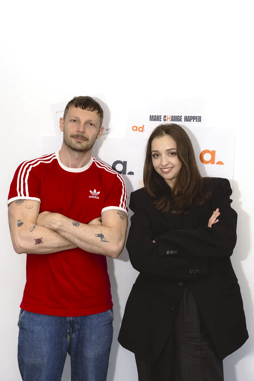 Mężczyzna w czerwonym t-shircie i kobieta w czarnej marynarce z założonymi rękami na białym tle.
