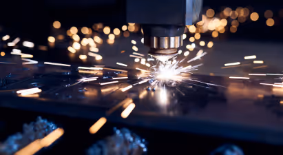 The image shows a laser cutting through metal, creating bright sparks as it works. The scene takes place outdoors at night, with the light from the laser illuminating the surroundings. The overall atmosphere is dynamic and captivating due to the contrast of light and darkness.