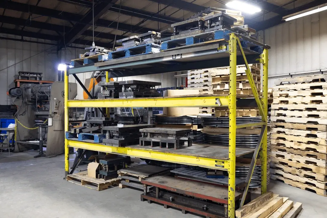 Heavy metal dies stored on yellow industrial shelving in a factory warehouse.