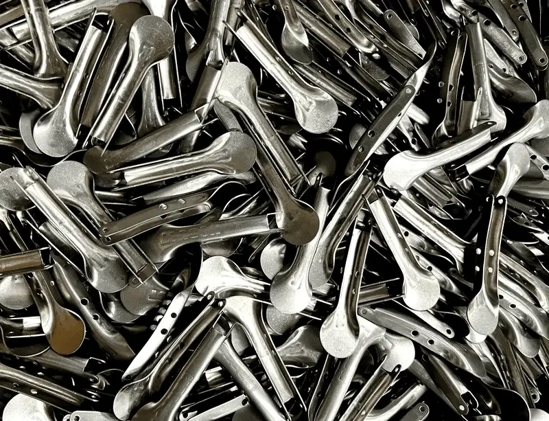 Pile of stamped metal parts stacked together, showing shiny, curved components in a manufacturing bin.