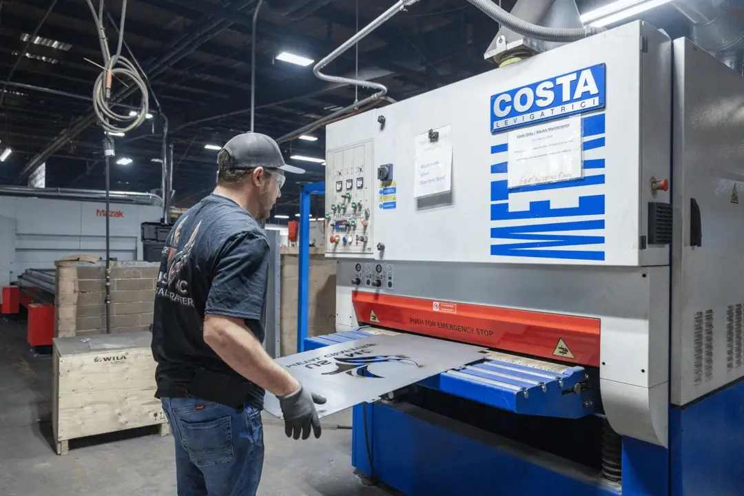 Worker in gloves and safety glasses operates a Costa Levigatrici industrial sanding machine with a metal sheet.