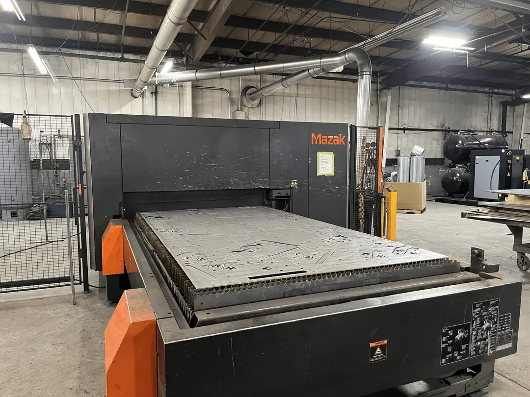 Optiplex 3015 Fiber Laser 8K laser cutter with a metal sheet featuring cut patterns inside an industrial workshop.
