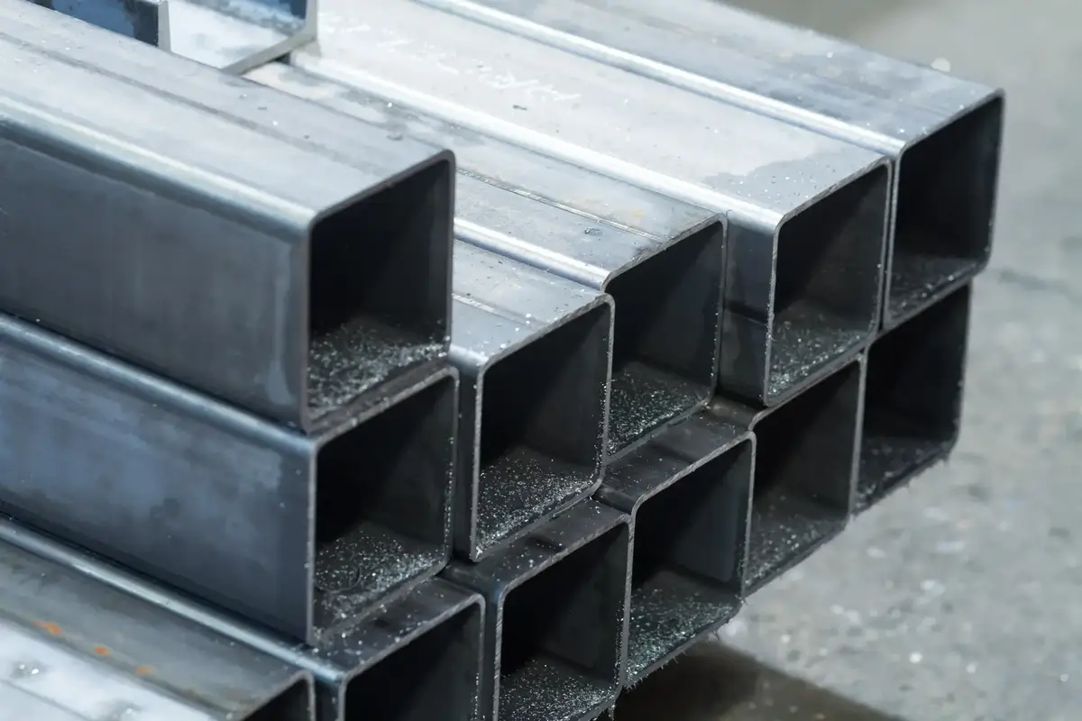 Stack of rectangular hollow carbon steel pipes with metallic surface and dust particles inside.