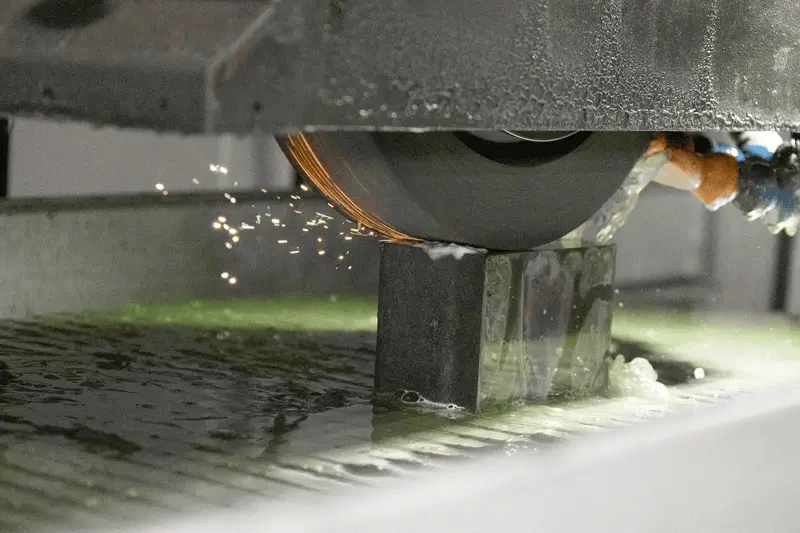 Industrial cutting machine slicing a wet rectangular stone block with sparks flying.