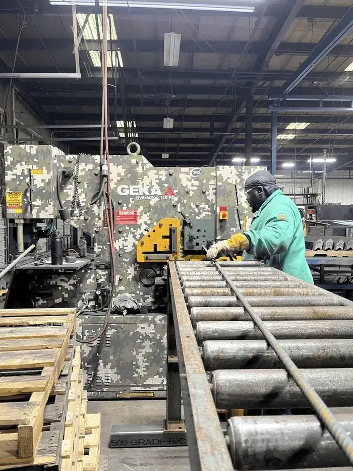 Worker in green protective gear operating a GEKA Hydracrop 110 PD ironworker machine in an industrial workshop.
