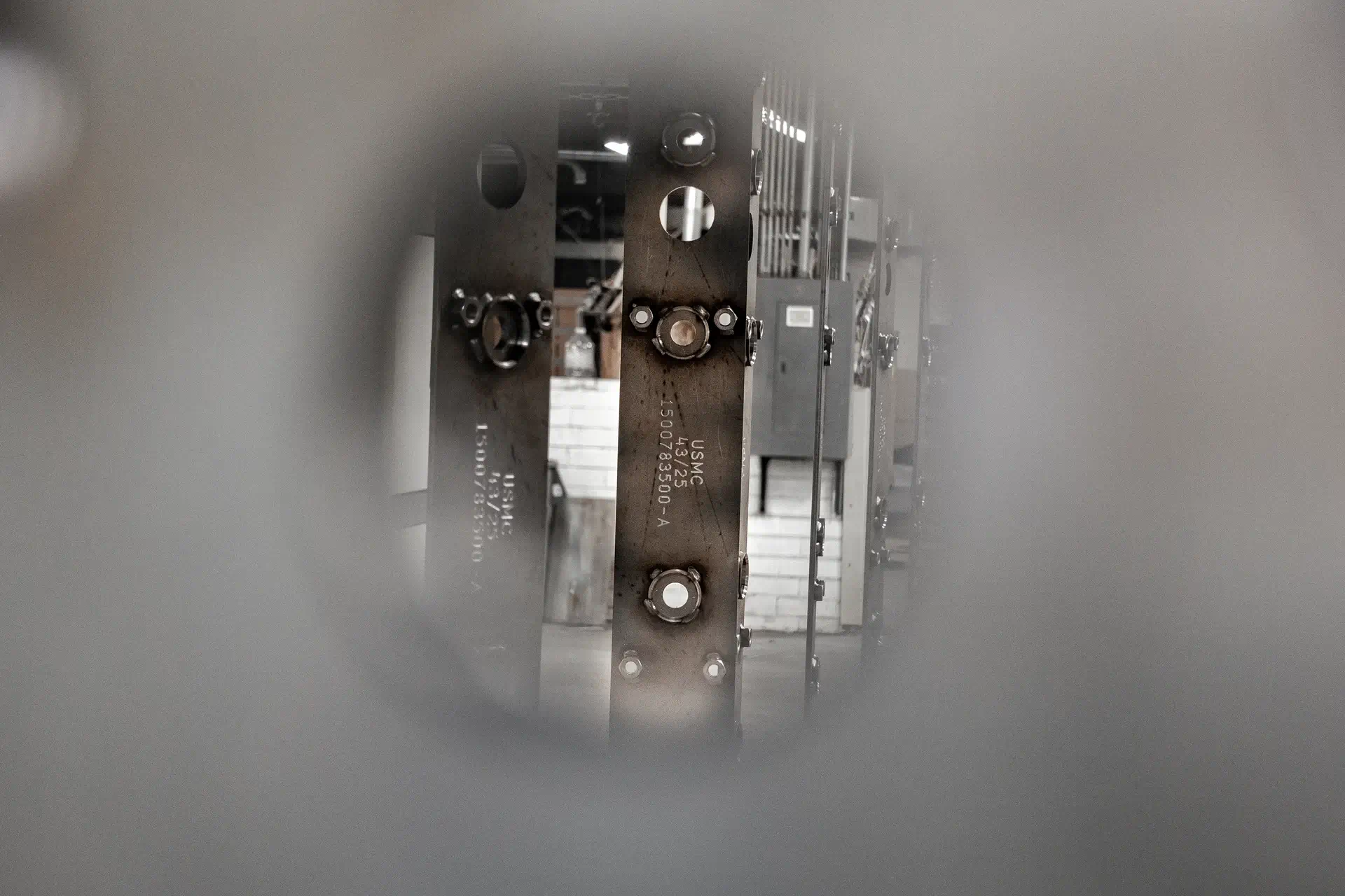 Metal structure with bolts and markings, viewed through a circular blurred frame in an industrial setting.