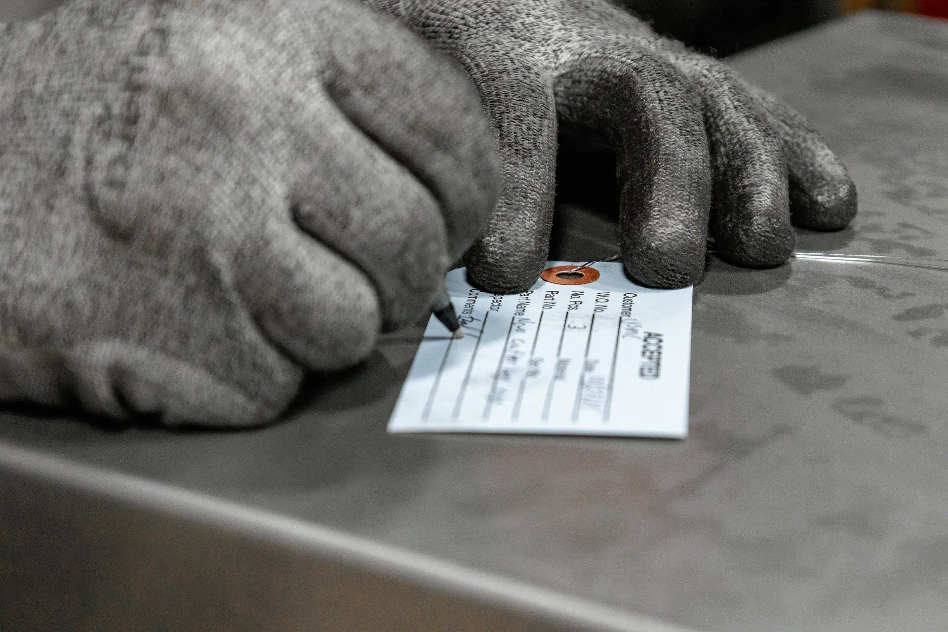 Gloved hand writing on a small white tag placed on a metal surface.