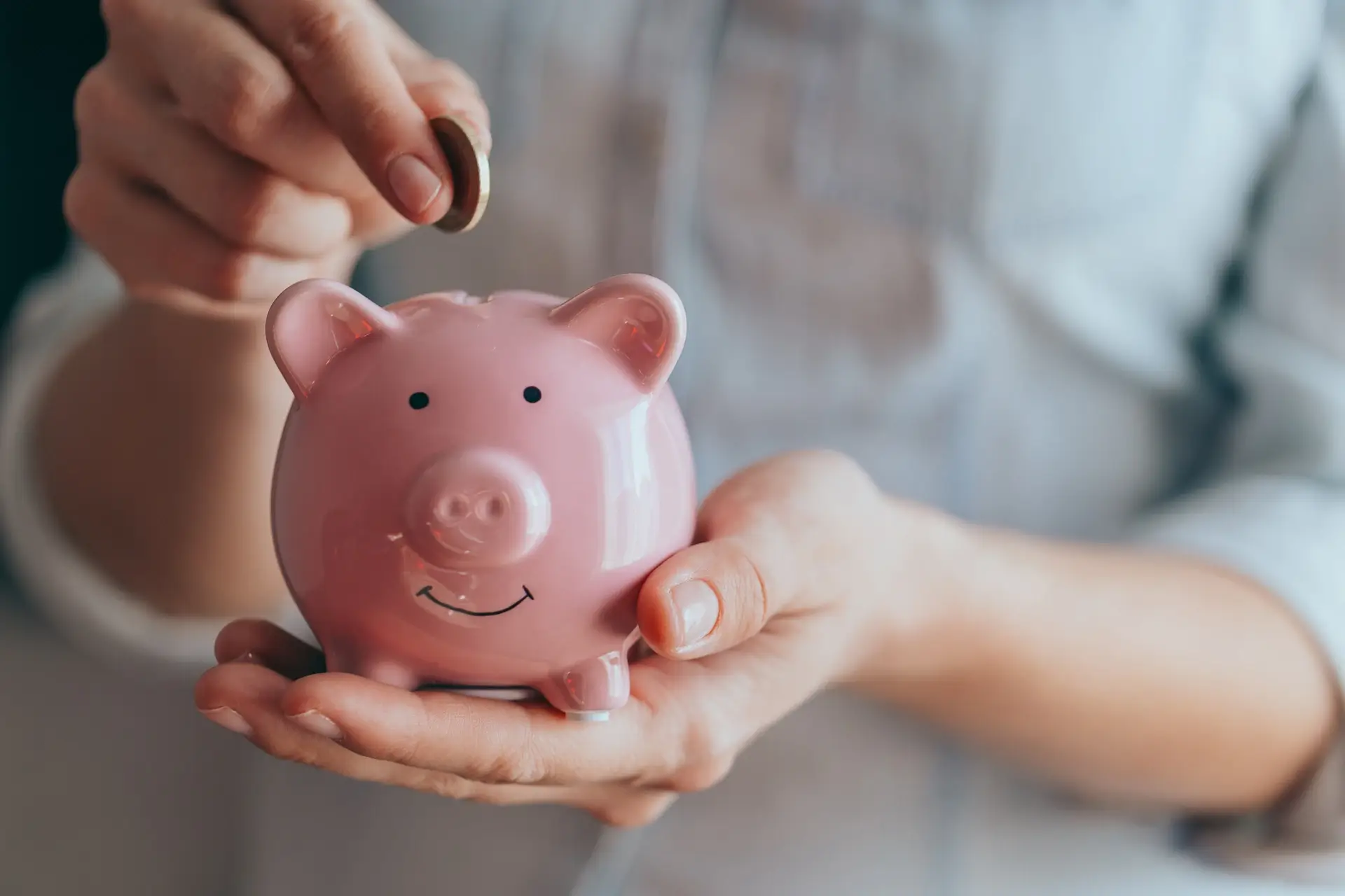 Person holding a pink piggy bank while inserting a coin.