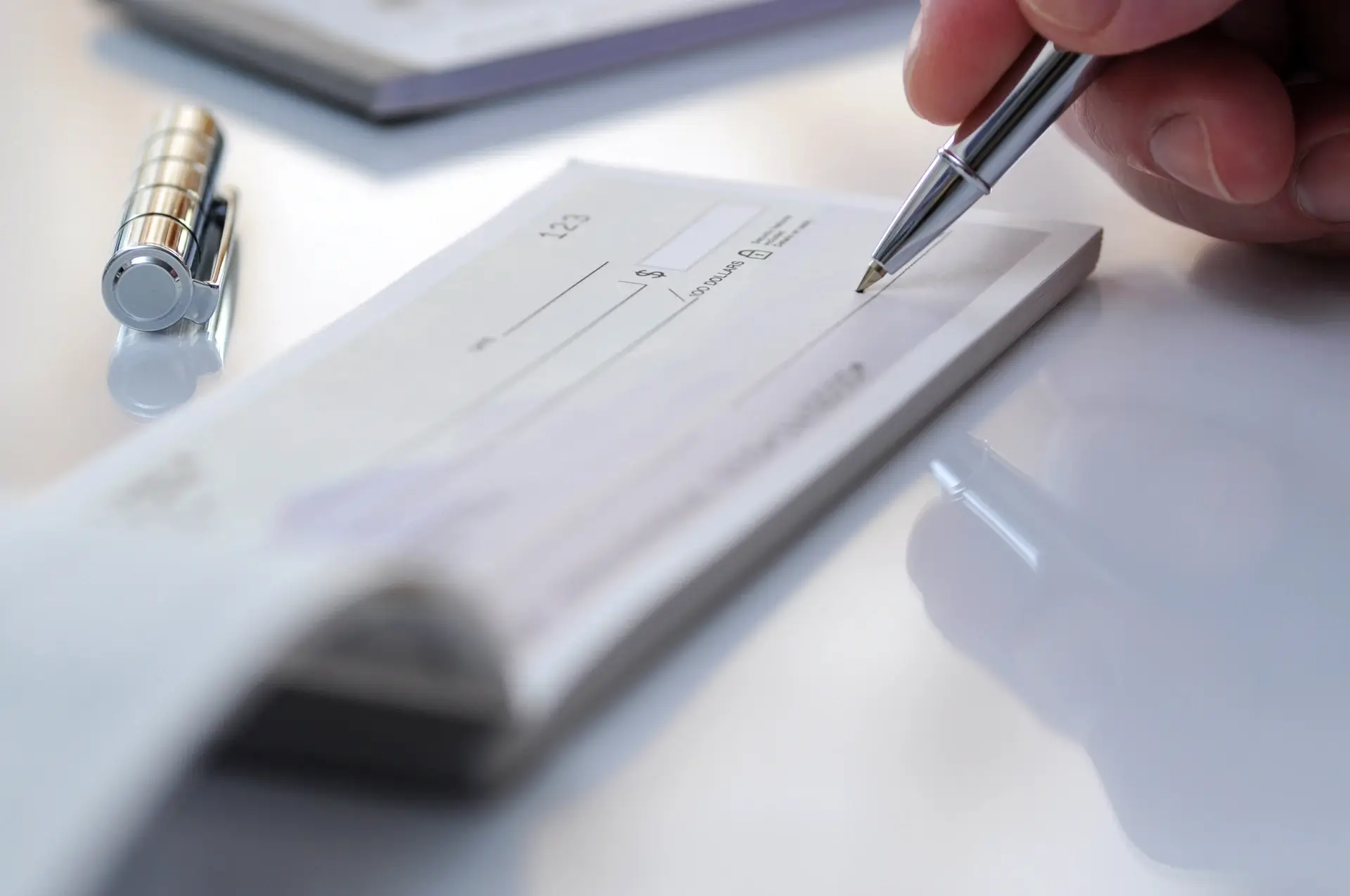 Hand holding a pen poised to write on a blank check placed on a white surface with a pen cap nearby.
