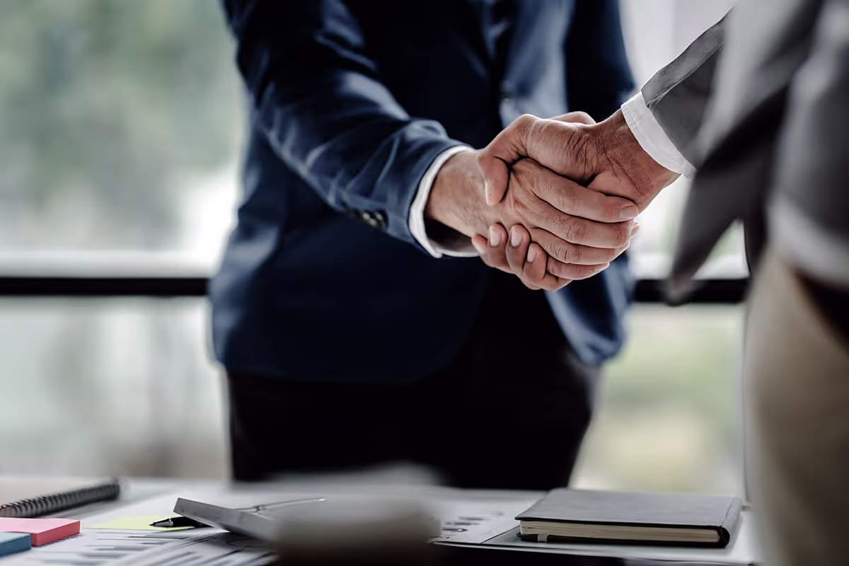 Two businessmen in suits shake hands in a office, signifying a business agreement or partnership.