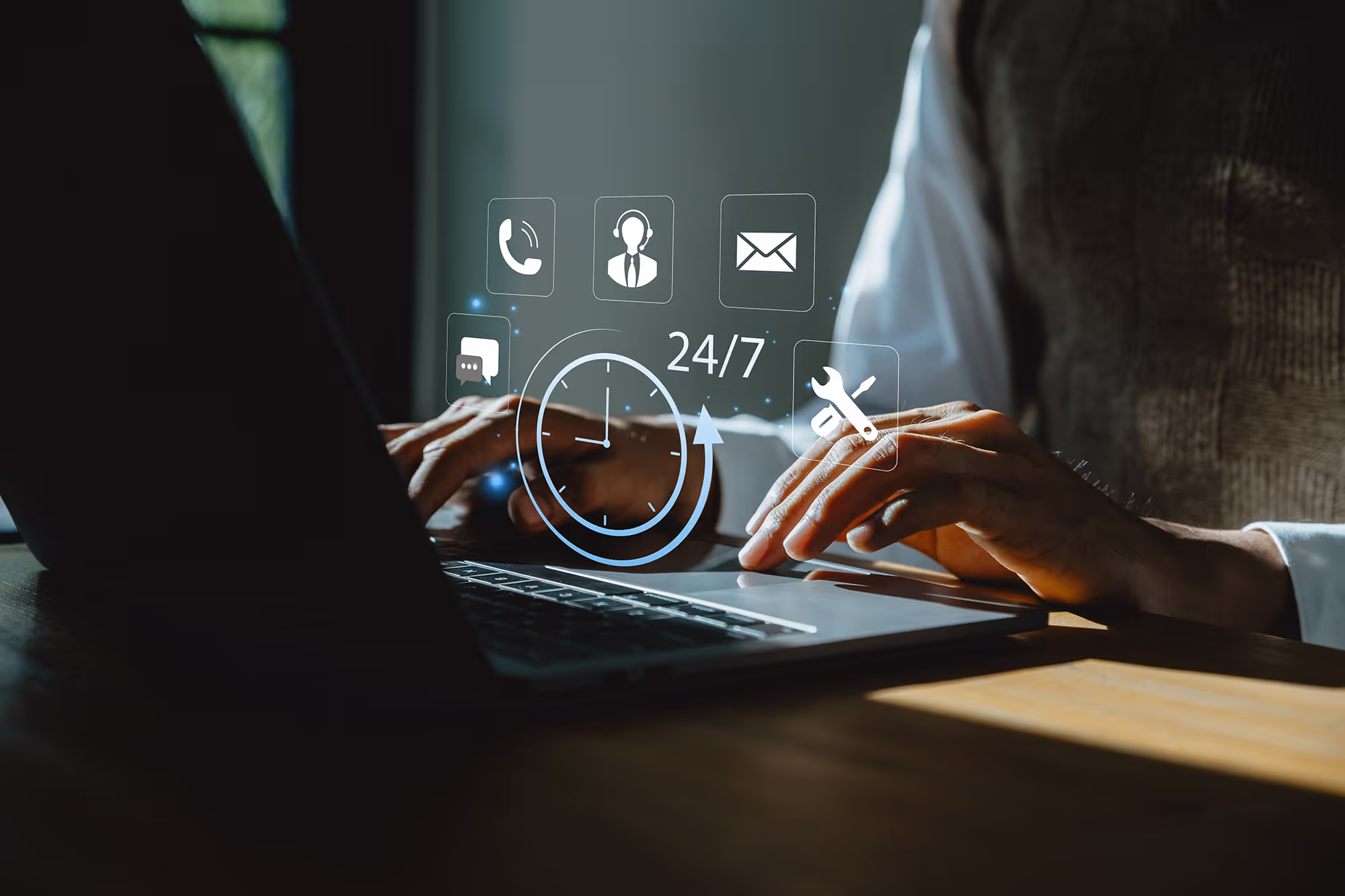 A person's hands are on the laptop keyboard, working and a graphic overlay is visible on the laptop screen, indicating 24/7 support.