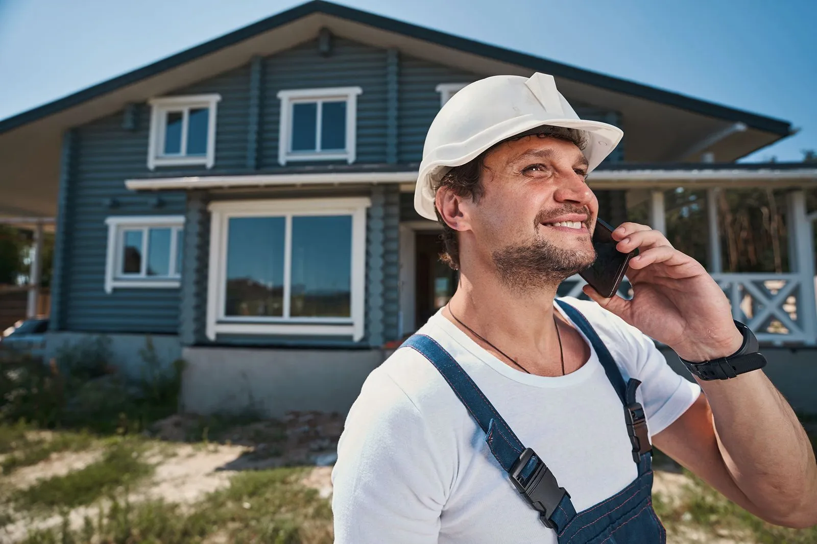 A handyman talking on the phone in front of a house.