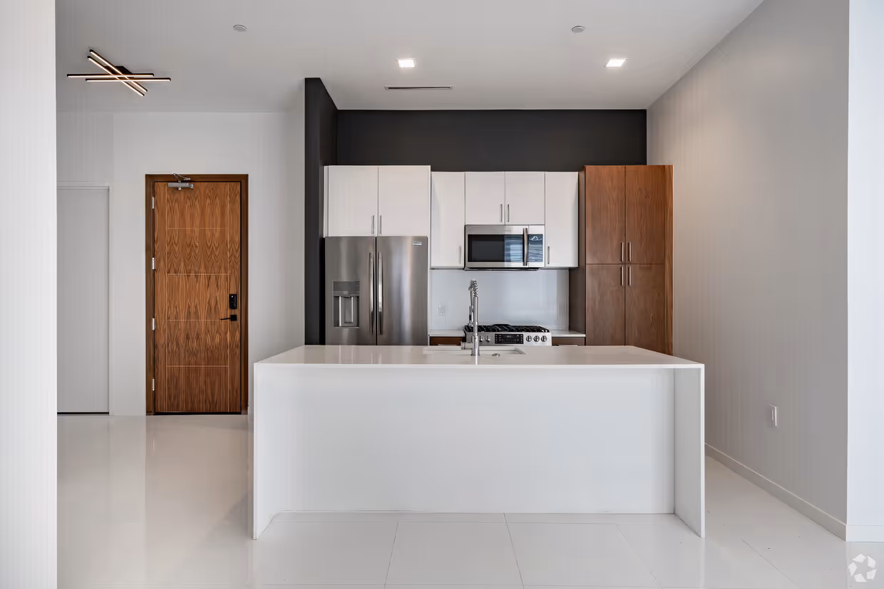 Modern kitchen with white island, stainless steel refrigerator, microwave, and wood cabinets against a dark accent wall.