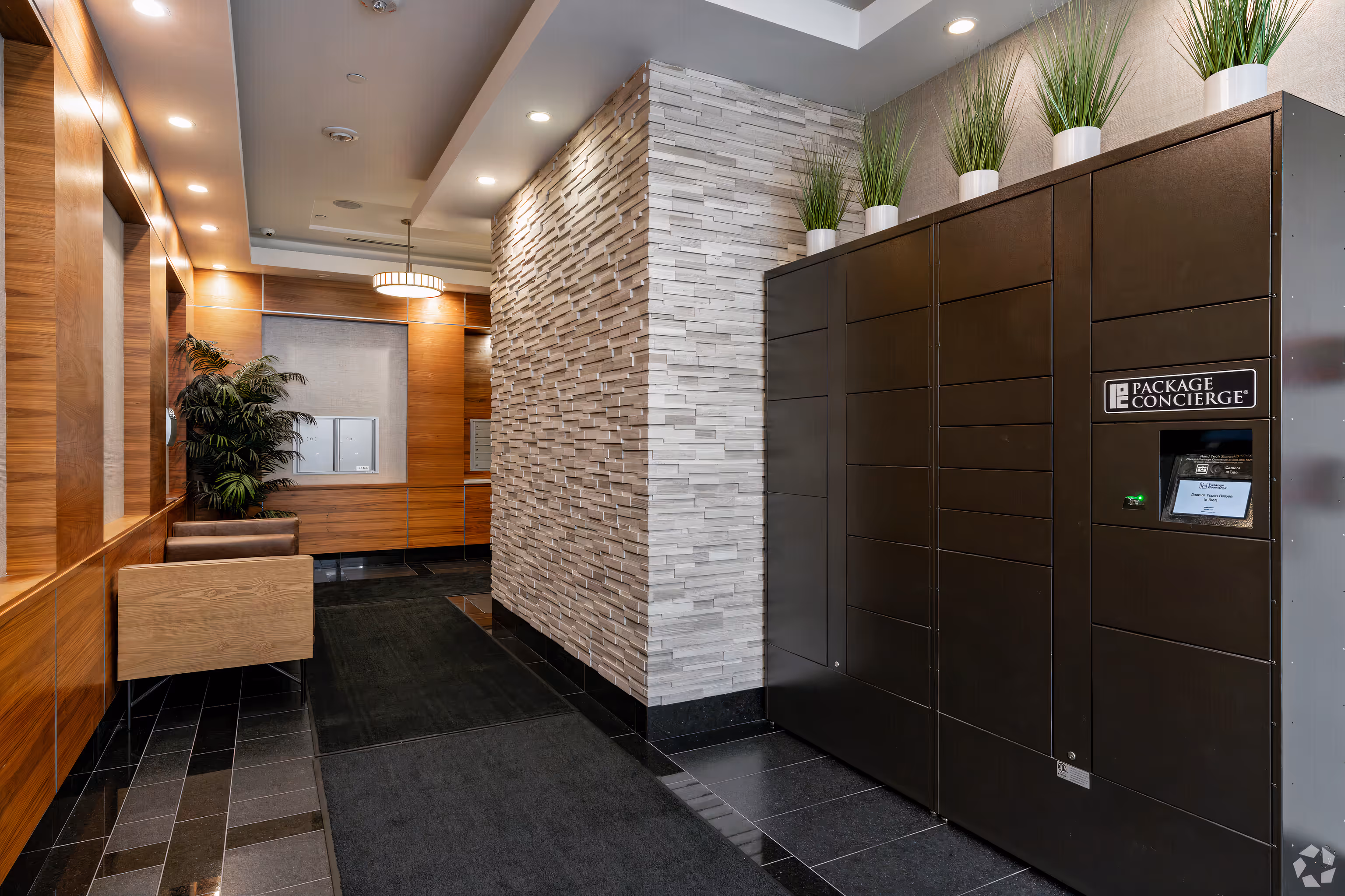 Modern lobby area with wooden panel walls, brown chairs, a plant, textured stone accent wall, and a black Package Concierge locker system topped with small potted plants.