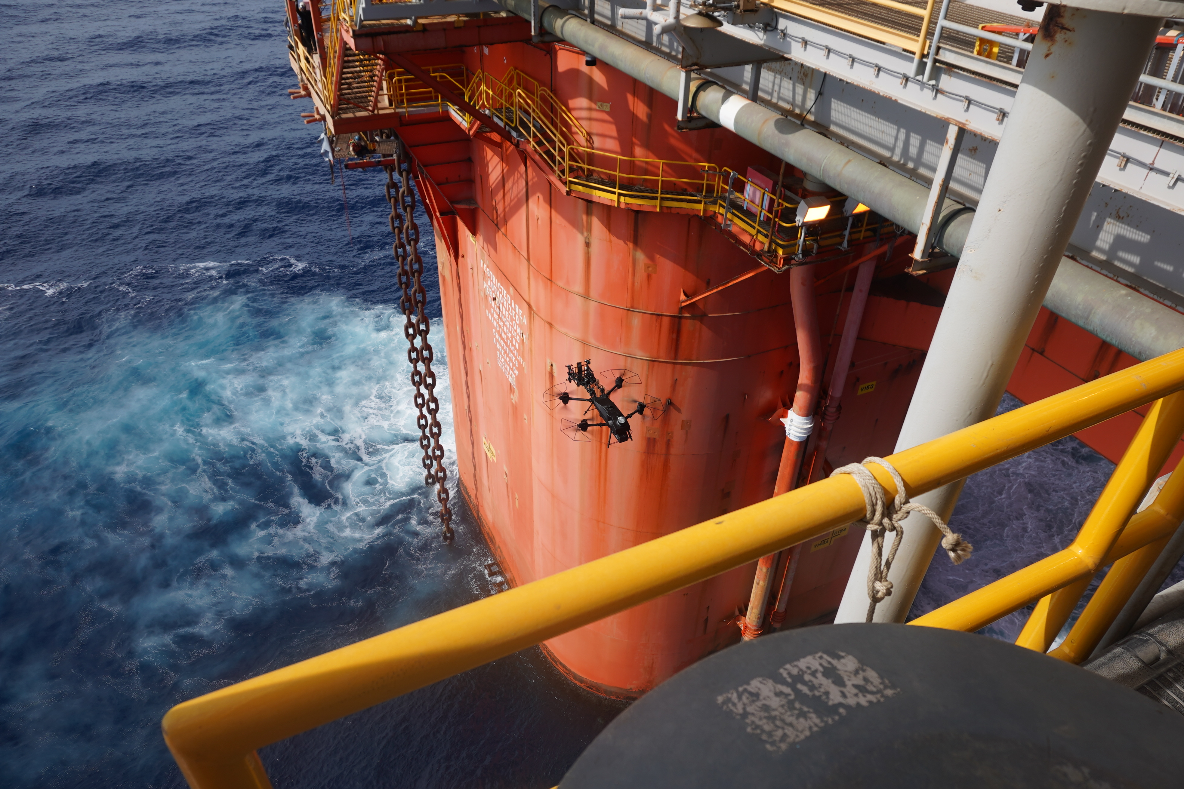 Drone flying near the orange platform of an offshore oil rig above the ocean.