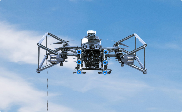 Front view of a large Avestec SKYRON2 drone with multiple cameras and propellers flying against a blue sky.
