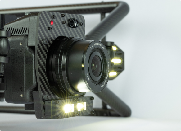 Close-up of a black camera on Avestec SKYRON2 drone with a wide-angle lens mounted on a stabilizing frame with attached lights.