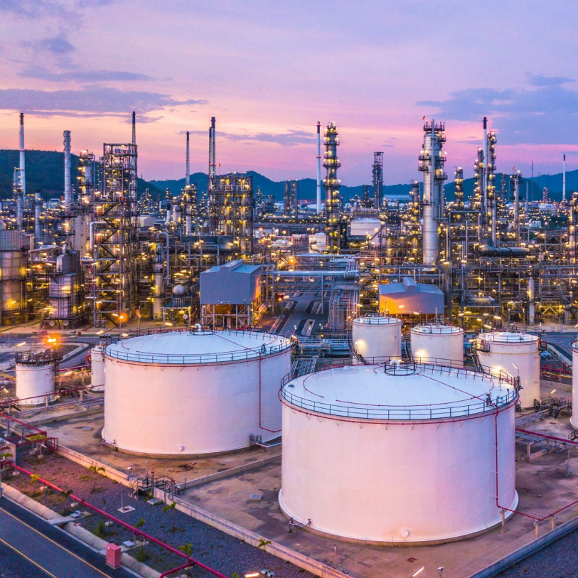 Petrochemical refinery with large white storage tanks and illuminated industrial towers at dusk.