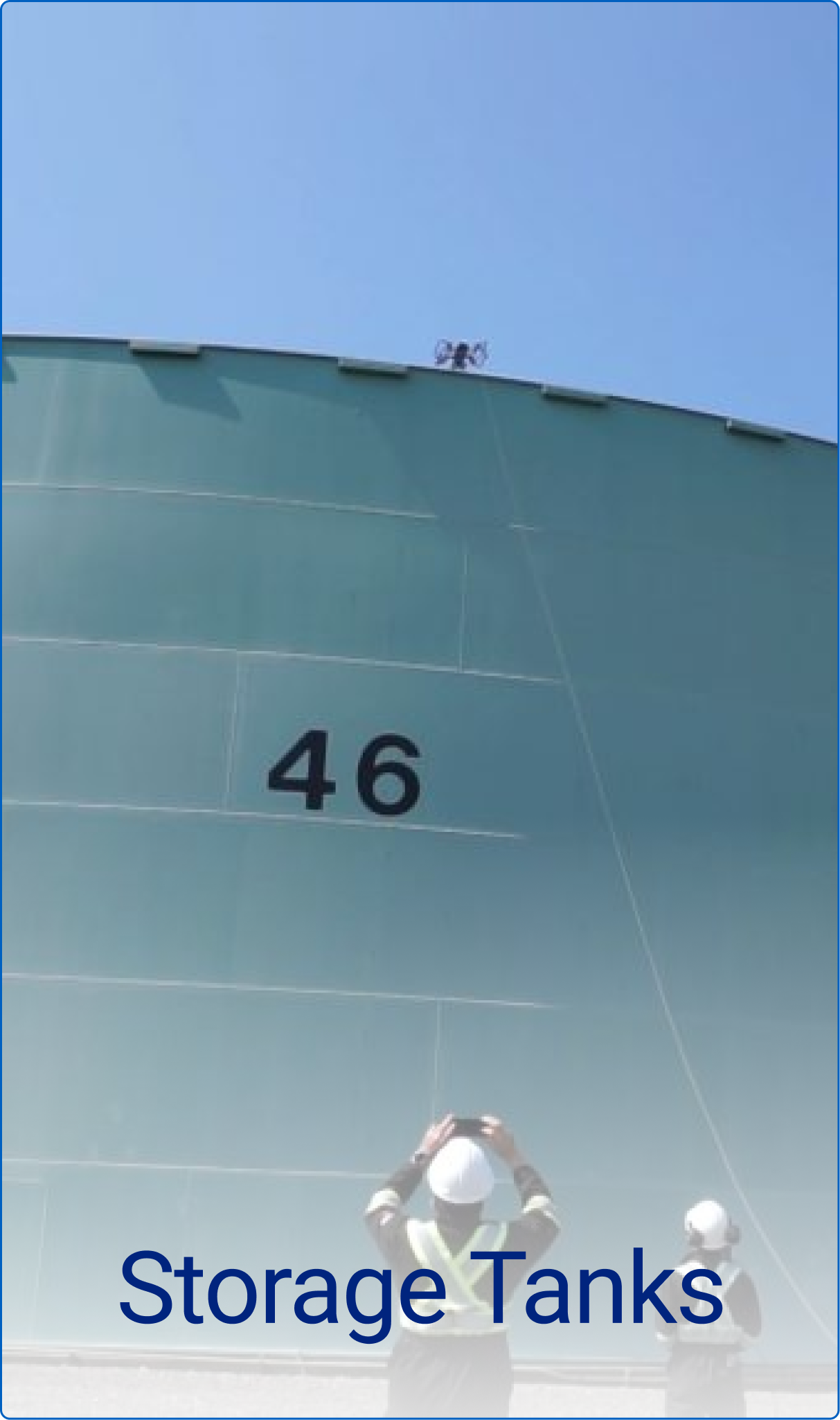 Large green industrial storage tank numbered 46 with two workers in safety gear observing it under a clear blue sky.