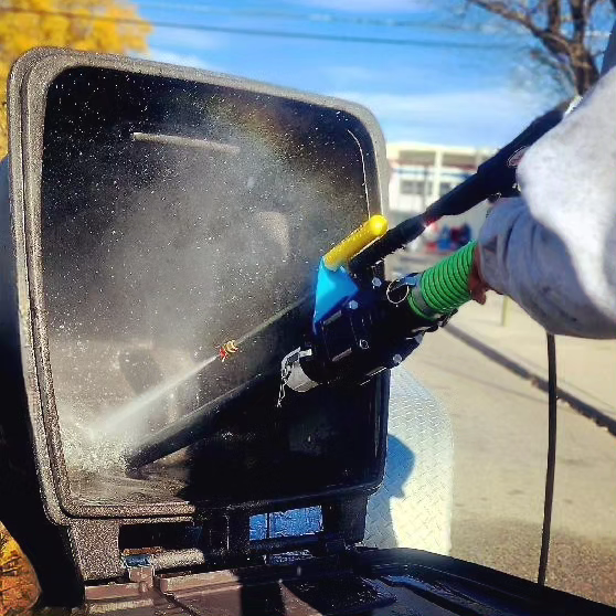Person power washing the inside of a large outdoor trash bin on a sunny day.
