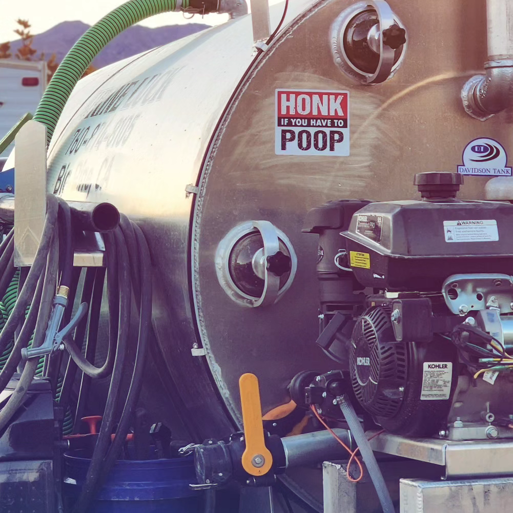 Close-up of a metal tanker with hoses and a motor, featuring a sticker that reads 'HONK IF YOU HAVE TO POOP'.
