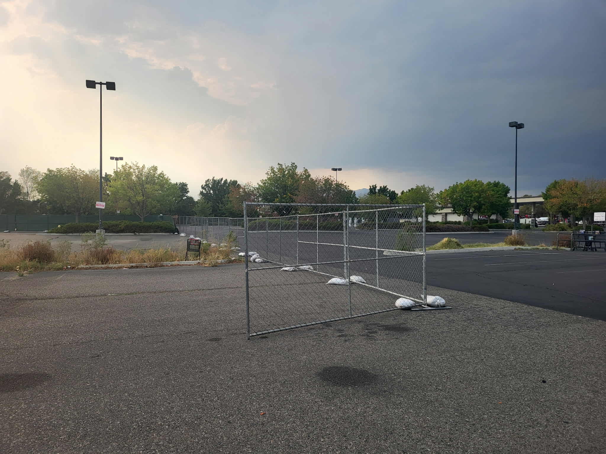 Empty parking lot with temporary chain-link fencing held down by sandbags under a cloudy sky.