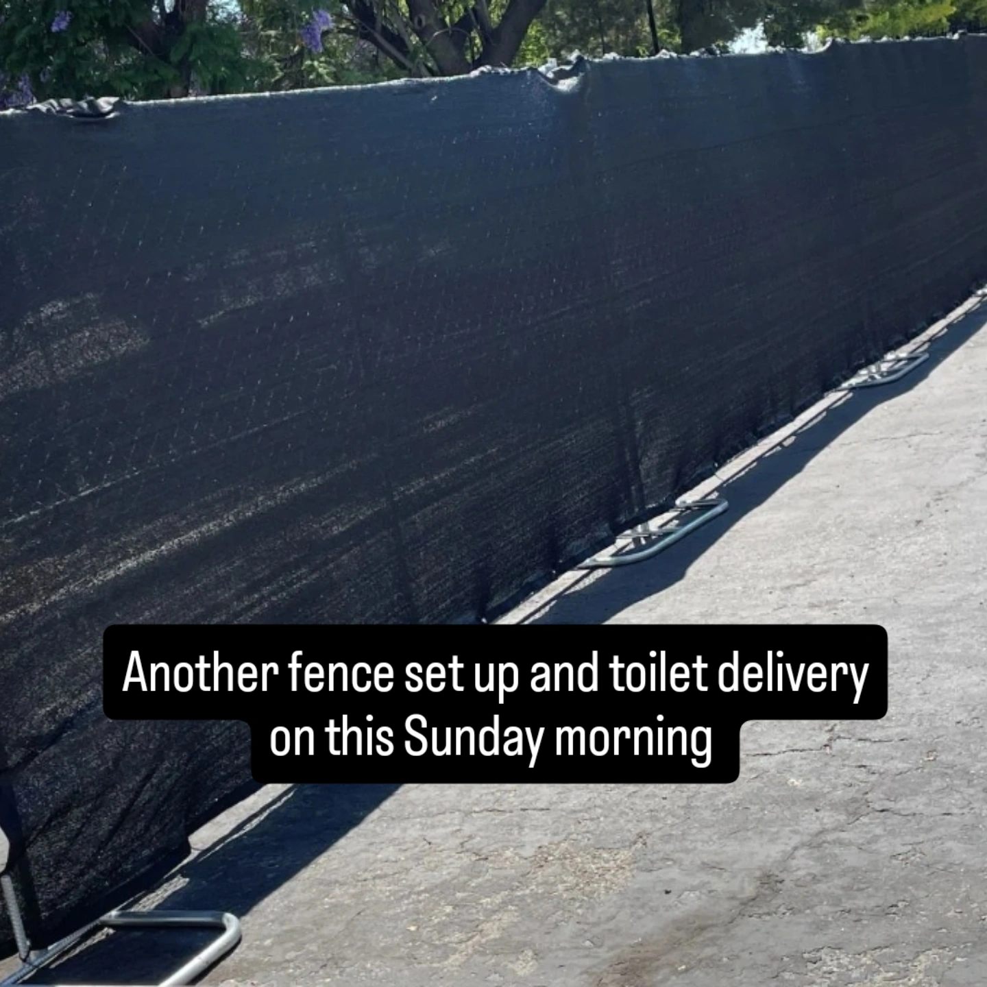 Long black mesh fence set up along a paved surface with trees in the background during daytime.