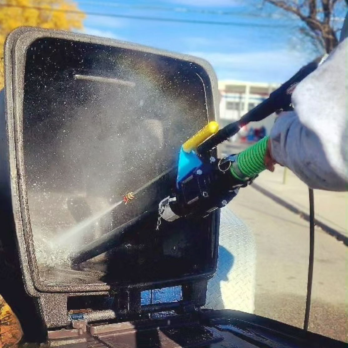 Person using a high-pressure water spray to clean the inside of a black container outdoors.