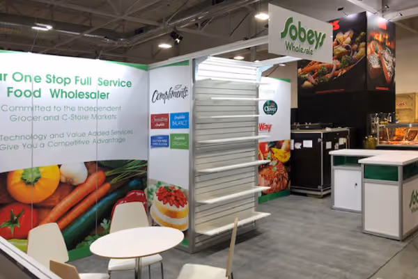 10x20 rental trade show booth for Sobey's groceries. The middle section extends outward with shelving to showcase retail products. At the top of the shelf extending towards the front of the booth is a sign panel with dimensional letters. The right of the b