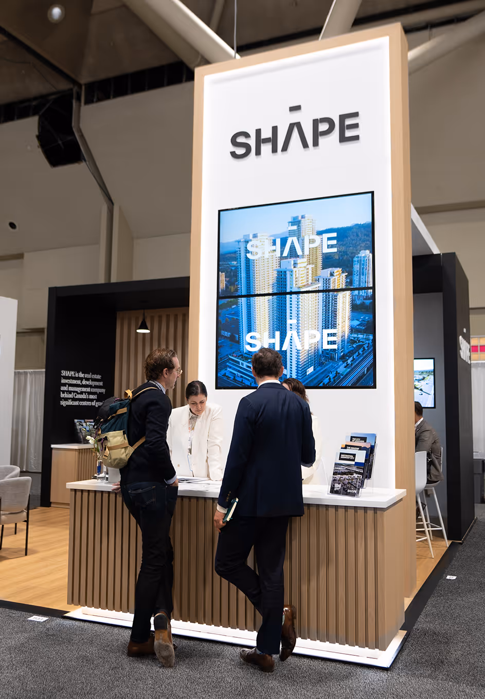 custom 20x20 trade show booth with group of 3 meeting at reception counter in front of media wall