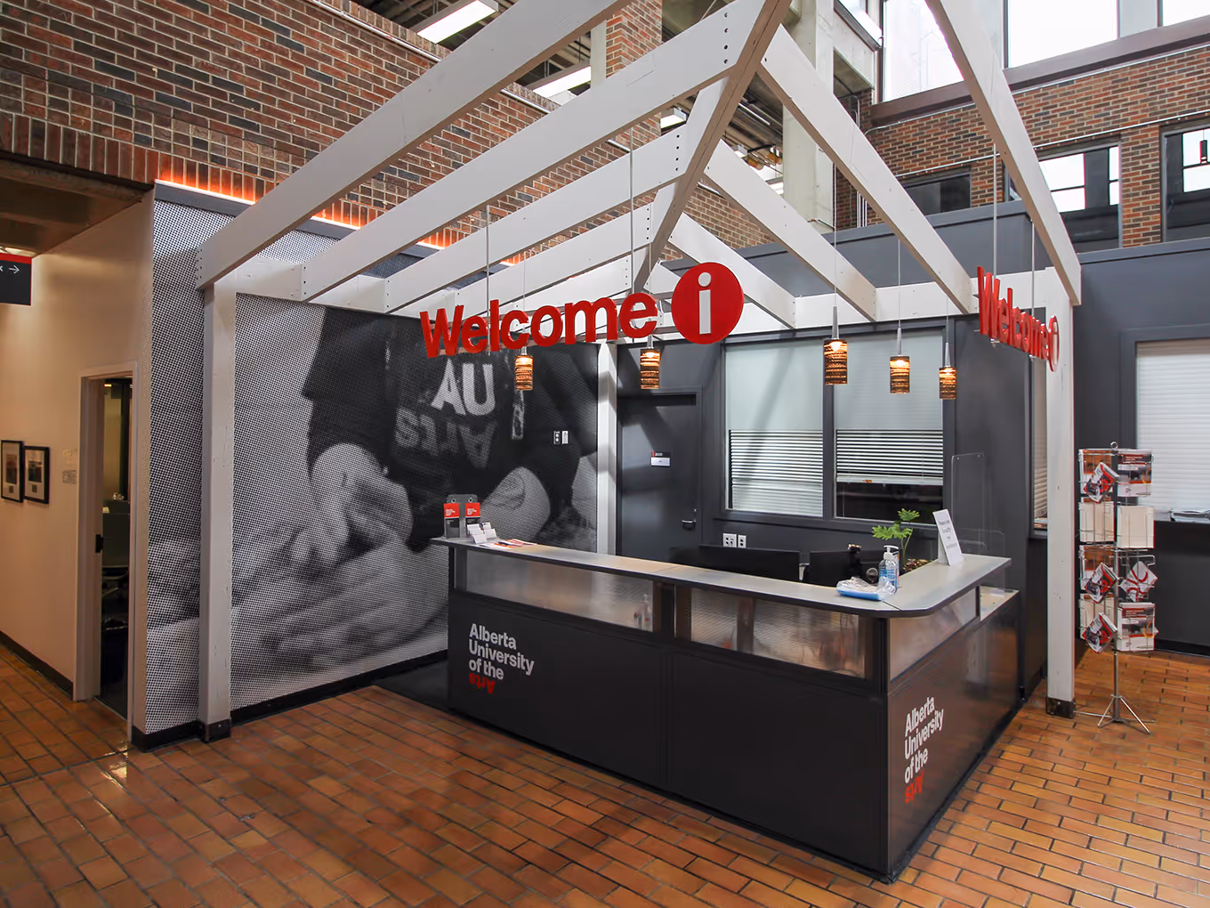 reception desk with suspended red welcome sign, black and white photo mural, and white wooden canopy