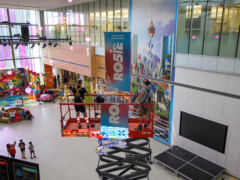 science centre open lobby with installers hanging vinyl banners for an exhibit.