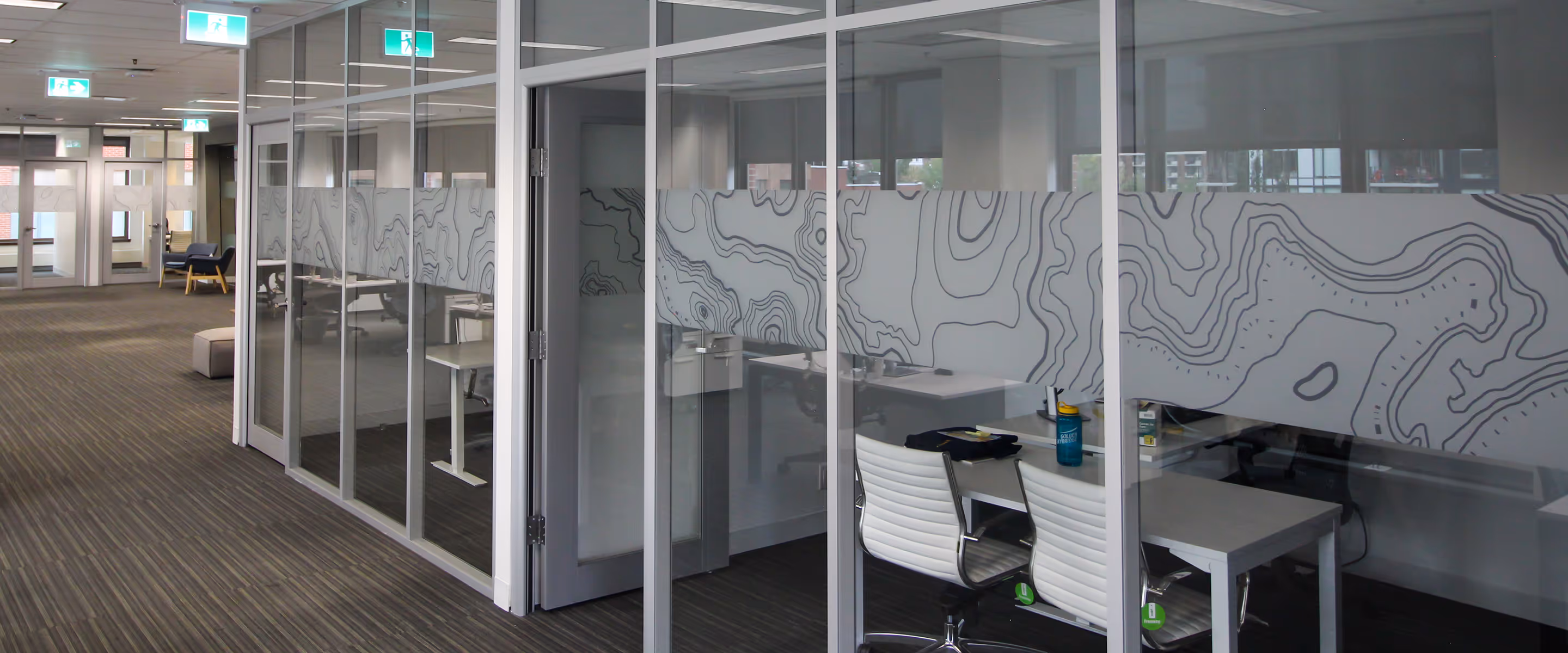 Glass-walled offices with silver topographic privacy film across doors and panels in Pursuit’s Calgary workspace.