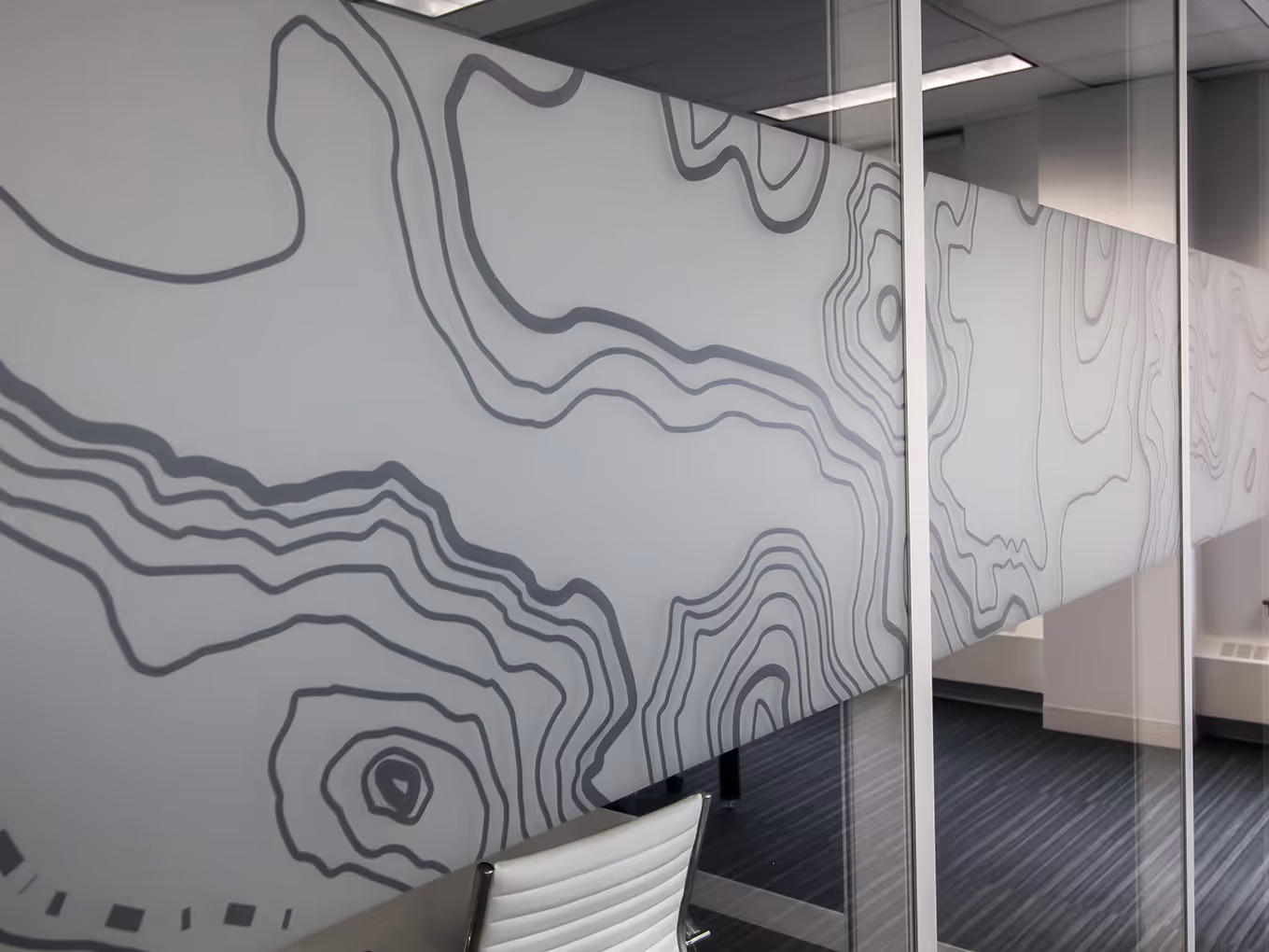 ngled view of topographic privacy film on glass office wall with contour-map pattern.