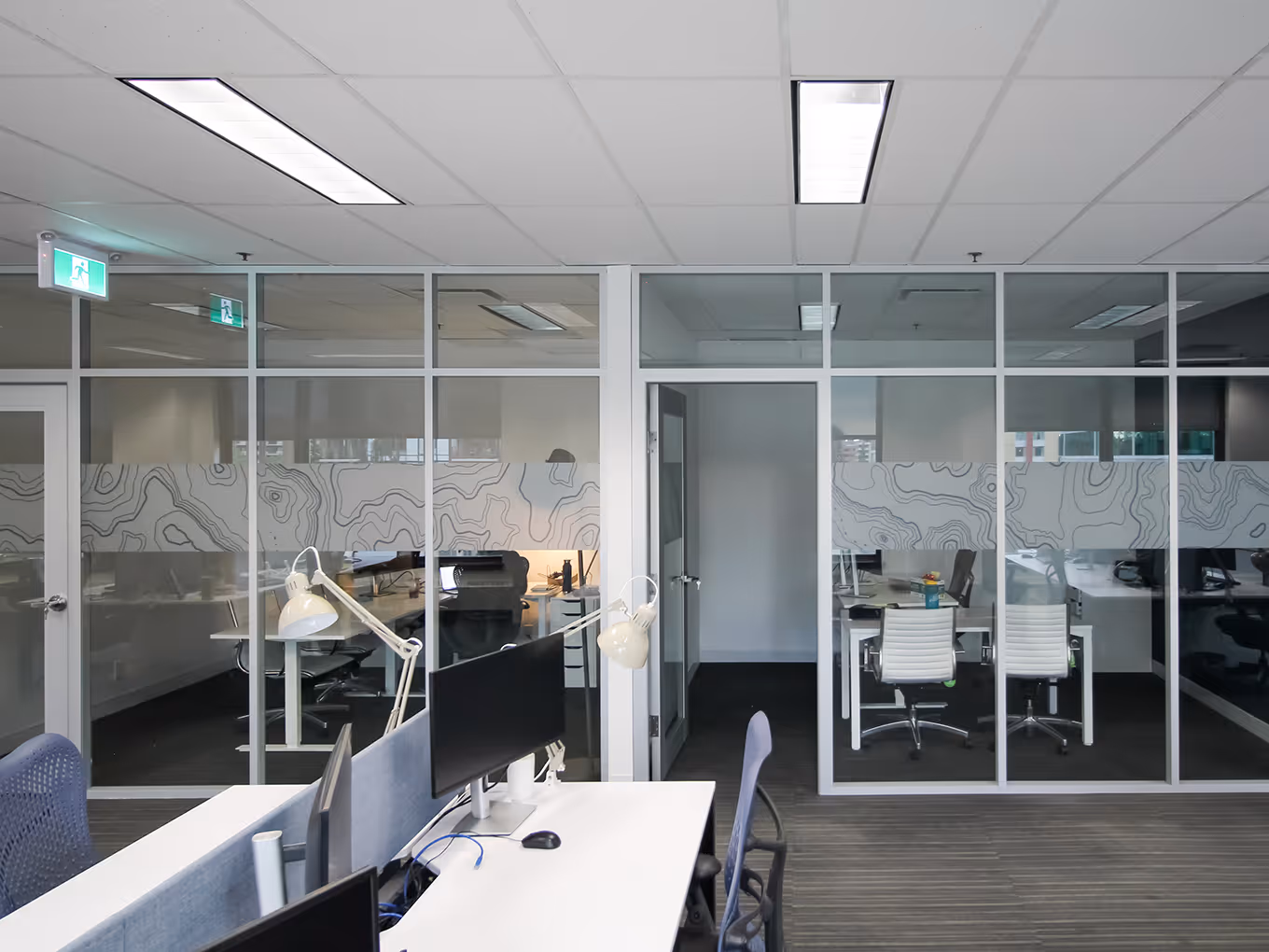 Open office sightline with glass partitions and etched topographic vinyl maintaining privacy.