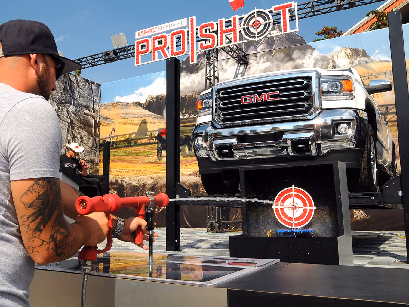 Guest plays the GMC ProShot water-gun challenge, aiming at a lit target beneath a lifted Sierra HD truck.