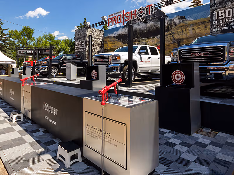 Row of ProShot water-gun stations facing multiple GMC Sierra HD trucks on hydraulically raised platforms.