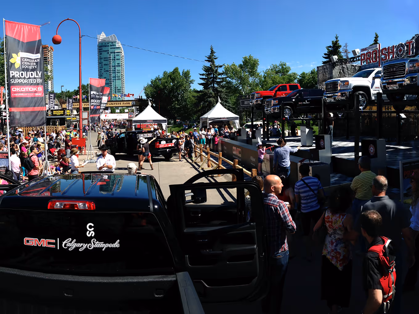 Large crowds gather around the GMC ProShot experiential exhibit featuring lifted trucks and branded staging.