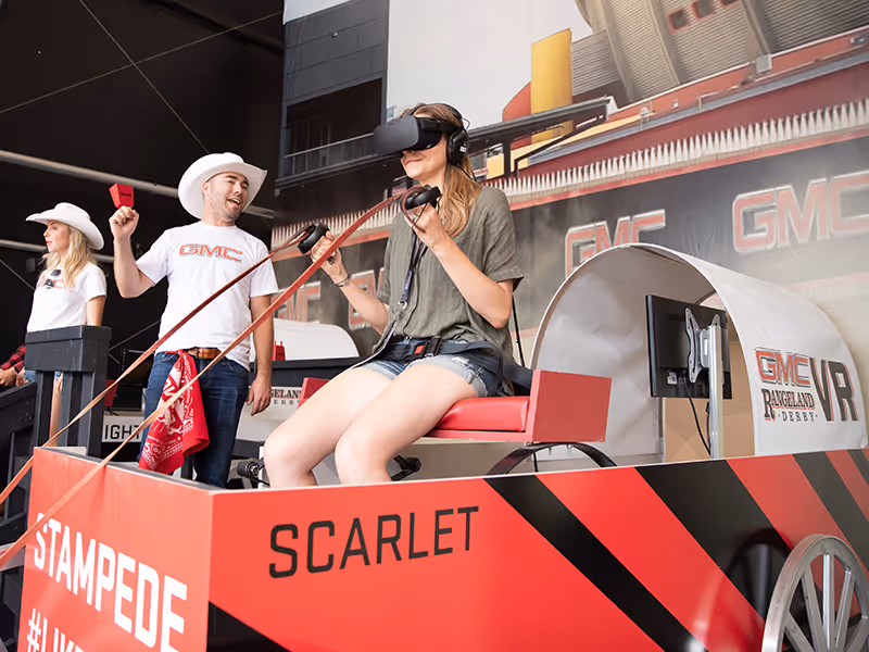 Participants use VR headsets while riding custom GMC-branded chuckwagon motion seats simulating a race.
